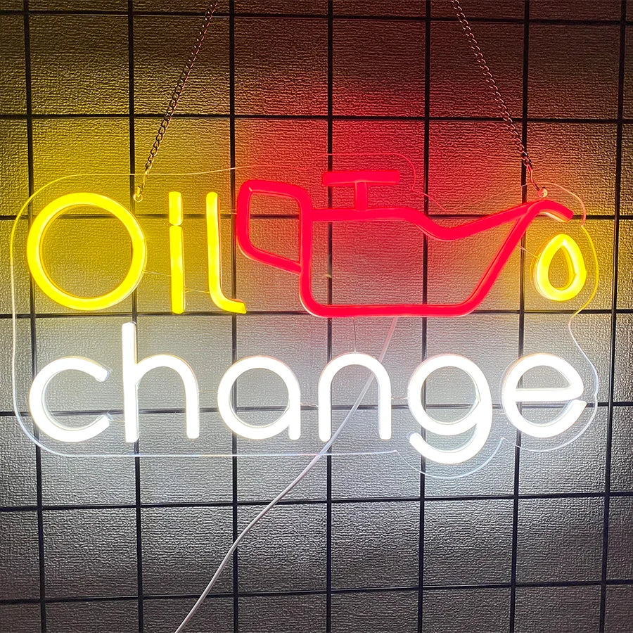 Neon sign spelling out Oil change in yellow and red lights against a dark grid background.