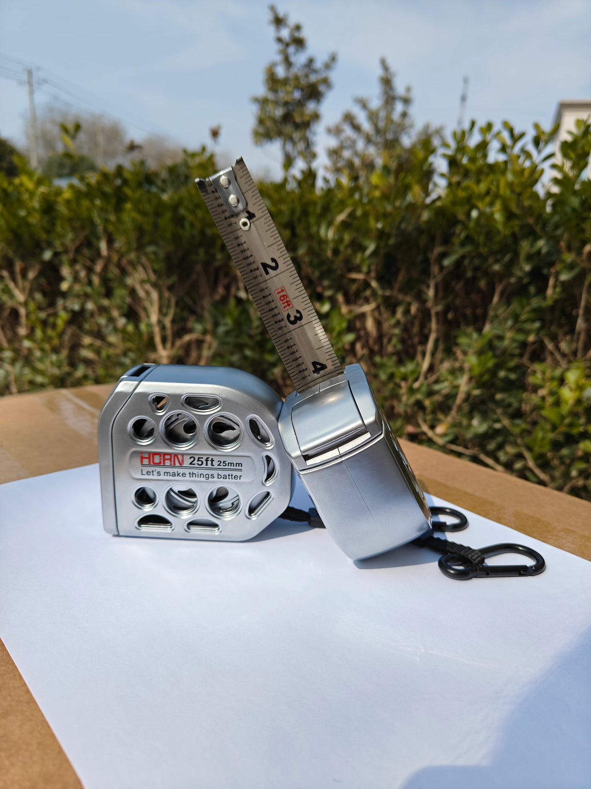 A silver metric tape measure is shown next to a ruler, resting on white paper.