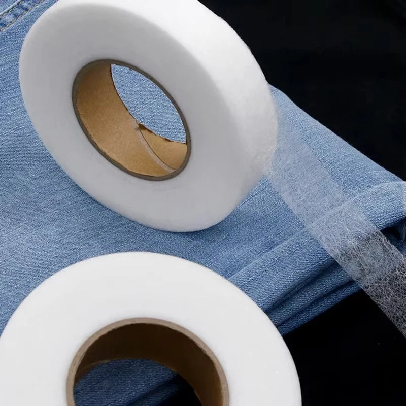 Rolls of white iron-on hemming tape for fabric edging placed on a blue cloth background.