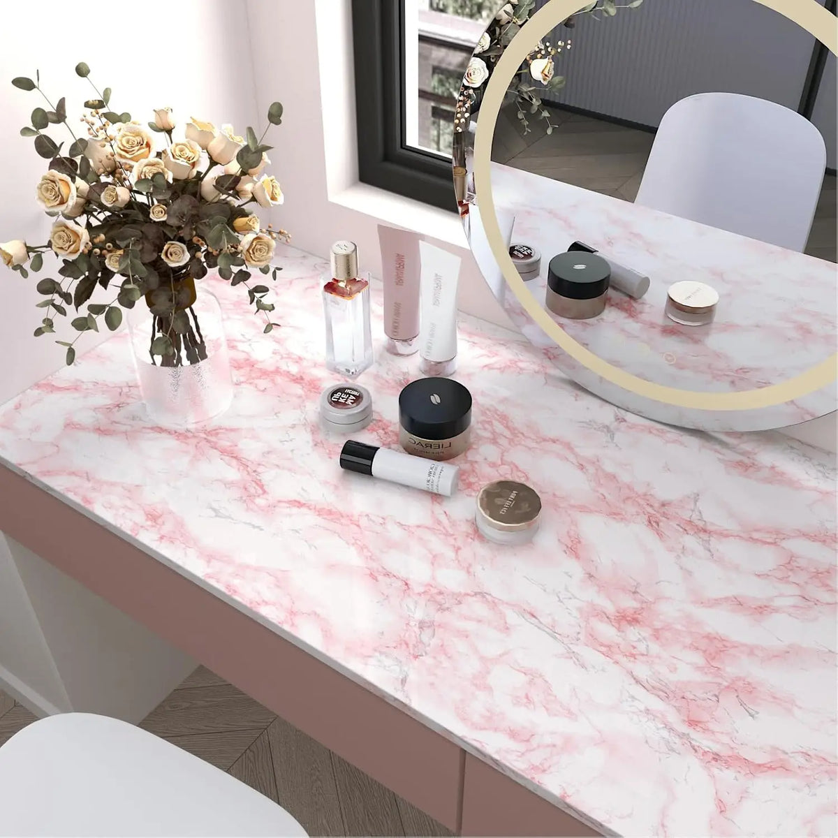 A display of cosmetic products on a pink marble countertop with a mirror and dried floral arrangement.