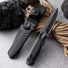 A black stainless steel fixed blade camping knife resting on a gray surface next to thick, natural rope.
