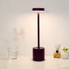 A modern, dark purple desk lamp with a cylindrical base and an adjustable light head illuminates a white surface.