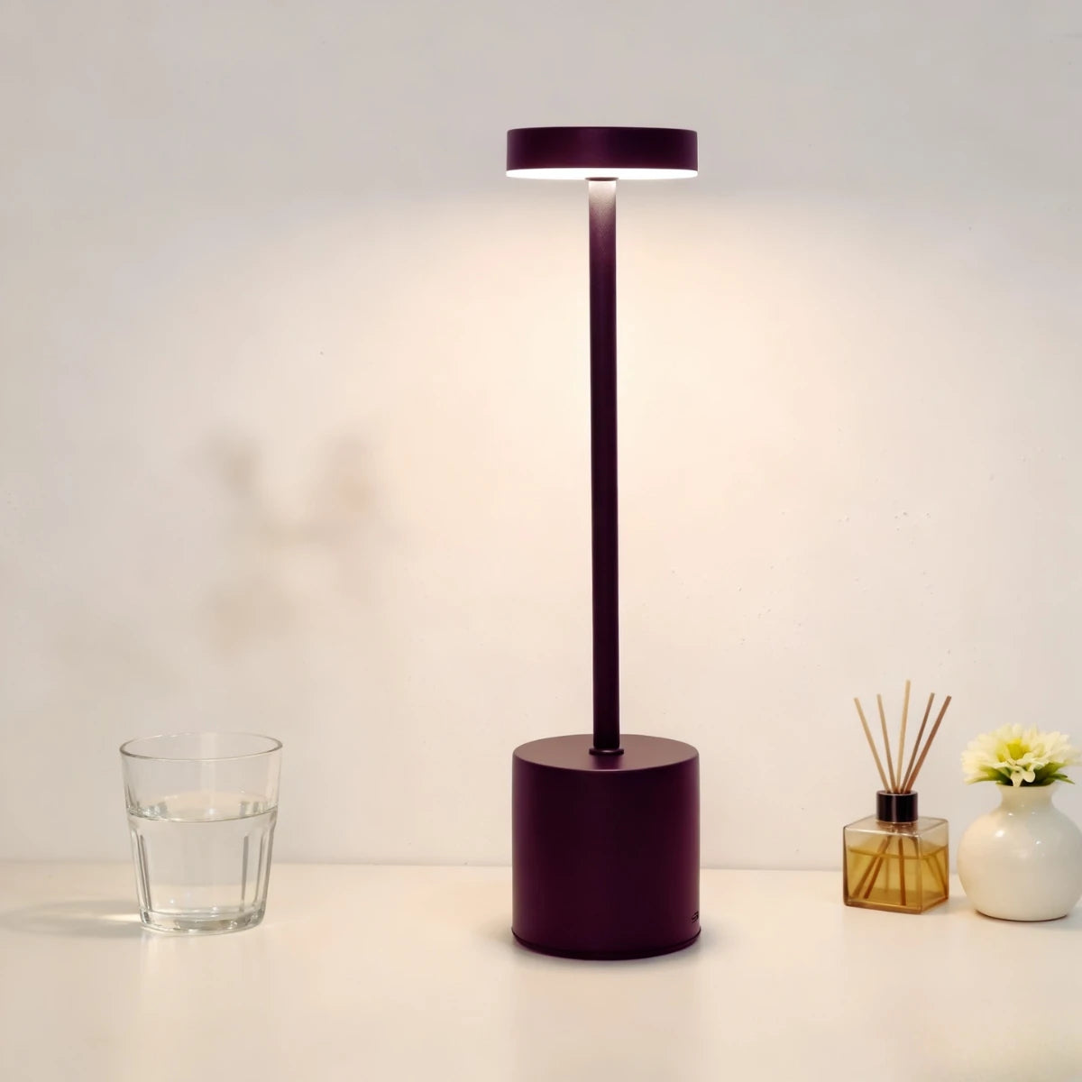 A modern, dark purple desk lamp with a cylindrical base and an adjustable light head illuminates a white surface.