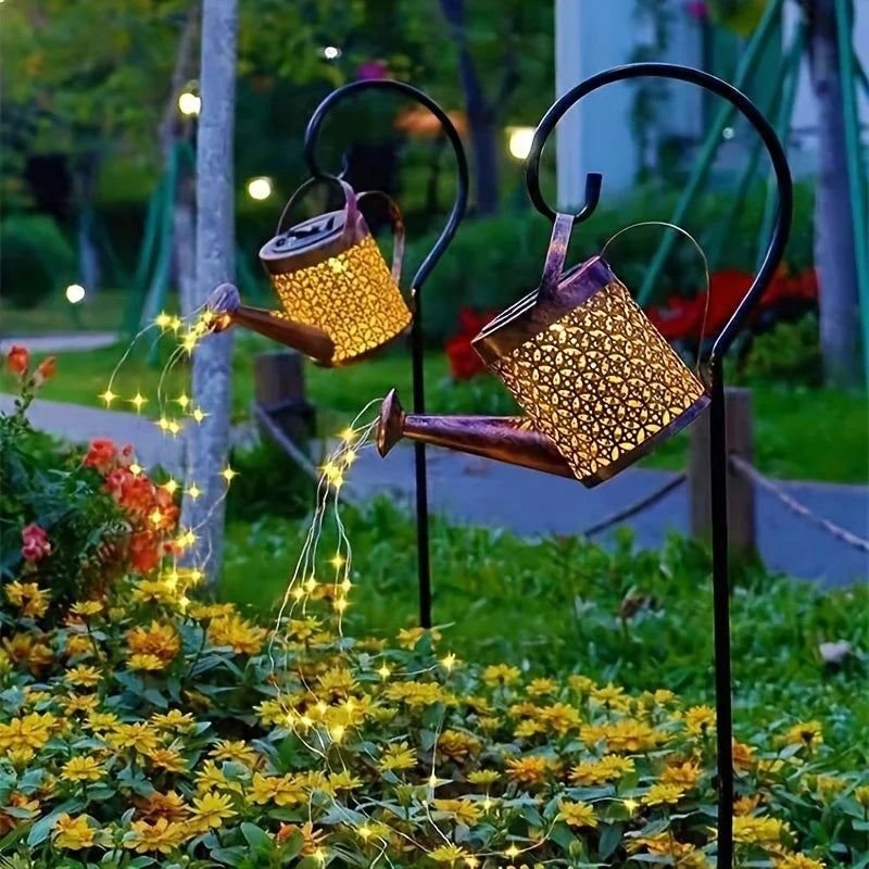 A brass solar fairy watering can light with glowing string lights watering yellow flowers in a garden.