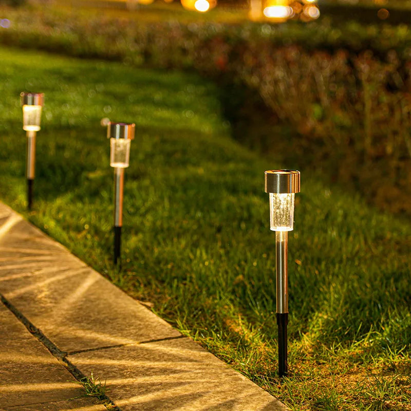 A row of solar powered outdoor garden lanterns lining a pathway in a grassy garden at dusk.
