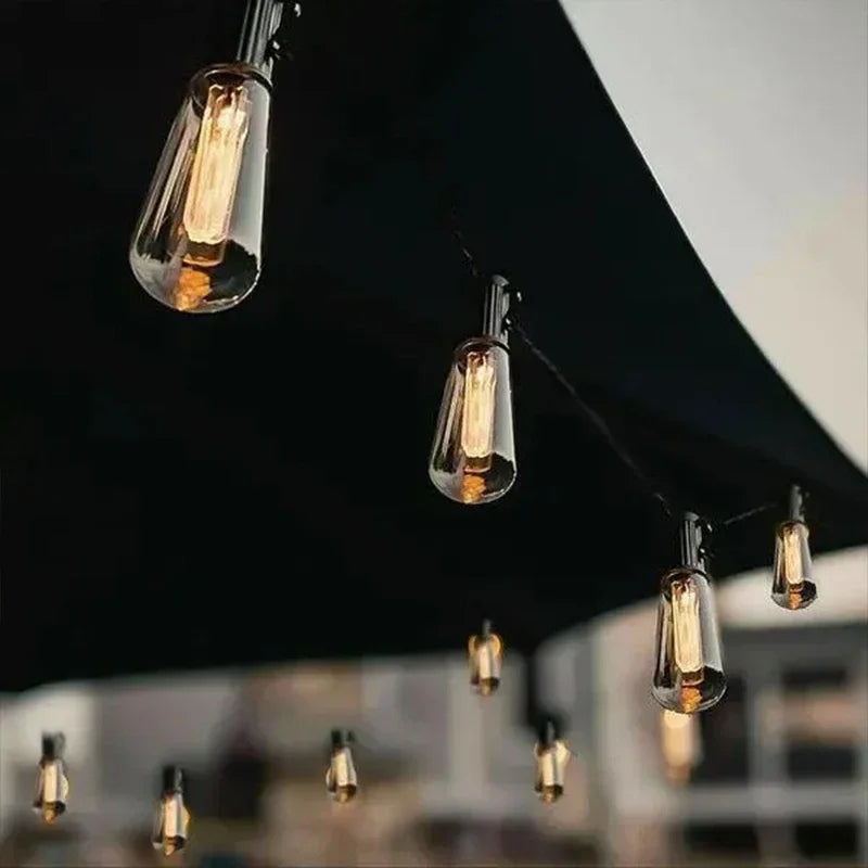 Lichterketten mit warm leuchtenden Glühbirnen unter einem dunklen Vordach.