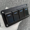 Panneau de commutateur en aluminium noir avec quatre interrupteurs individuels, posé sur une surface en tissu gris.