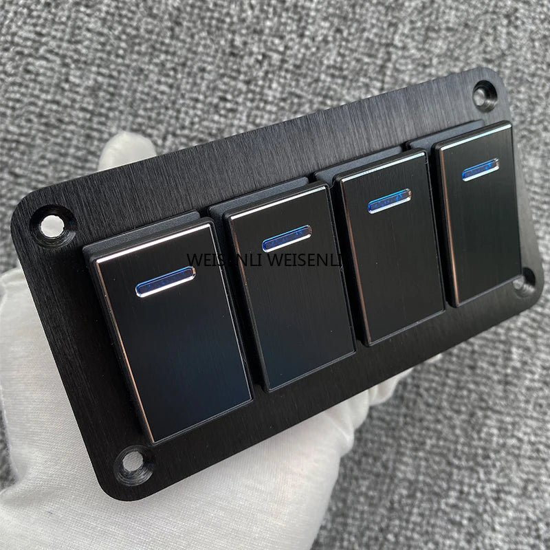 Panneau de commutateur en aluminium noir avec quatre interrupteurs individuels, posé sur une surface en tissu gris.