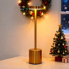 A brass desk lamp with a gold base and adjustable arm illuminates a festive wreath and Christmas tree.