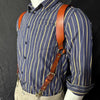A man wearing a blue striped shirt with brown leather double shoulder suspenders.