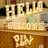 Exhibición de letras LED blancas iluminadas que deletrean HELLO WELCOME and PLAY en una estantería de madera.