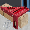 Règle triangulaire en aluminium rouge de précision posée sur un bloc en bois avec divers punaises métalliques à proximité.