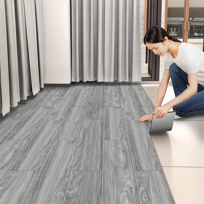 A woman is installing gray wood grain peel and stick floor tiles on a light floor in a modern room.