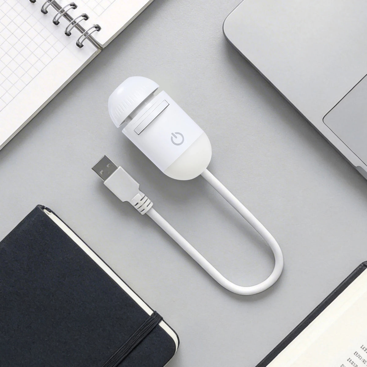 A white 2-in-1 Galaxy Star Projector night light with a cord rests on a gray surface next to a notebook and a spiral-bound pa