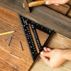 A hand is using a precision triangle square ruler for woodworking on a wooden surface.