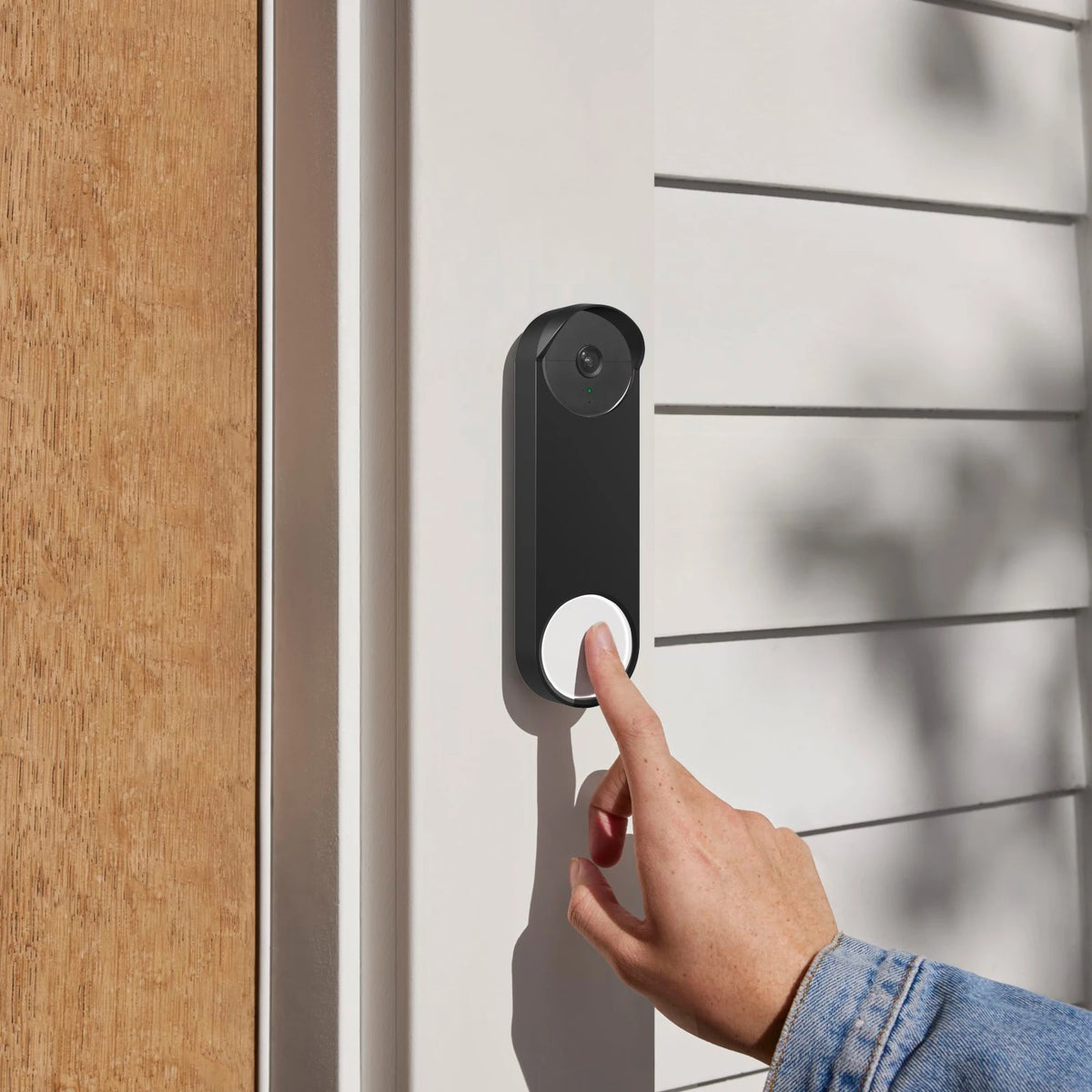 A hand is pressing a black weatherproof silicone cover on a white door panel to activate a doorbell.