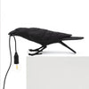 Eine schwarze Harfenschmuckvogelskulptur neben einer Glühbirne, die eine Tischlampen-Design andeutet.