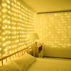 Un dormitorio con una cama iluminada por luces de guirnalda LED verticales, proyectando un cálido brillo amarillo en la pared