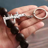 A hand holds a black beaded bracelet with a metal measuring ruler and caliper keychain attached.