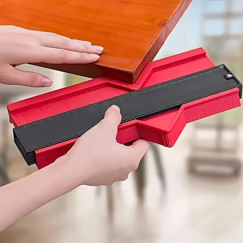 Hands are adjusting a red plastic contour measuring ruler with a black strip on an orange wooden surface.