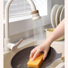 A hand is using an extendable tap filter sprayer to dispense water onto a frying pan.