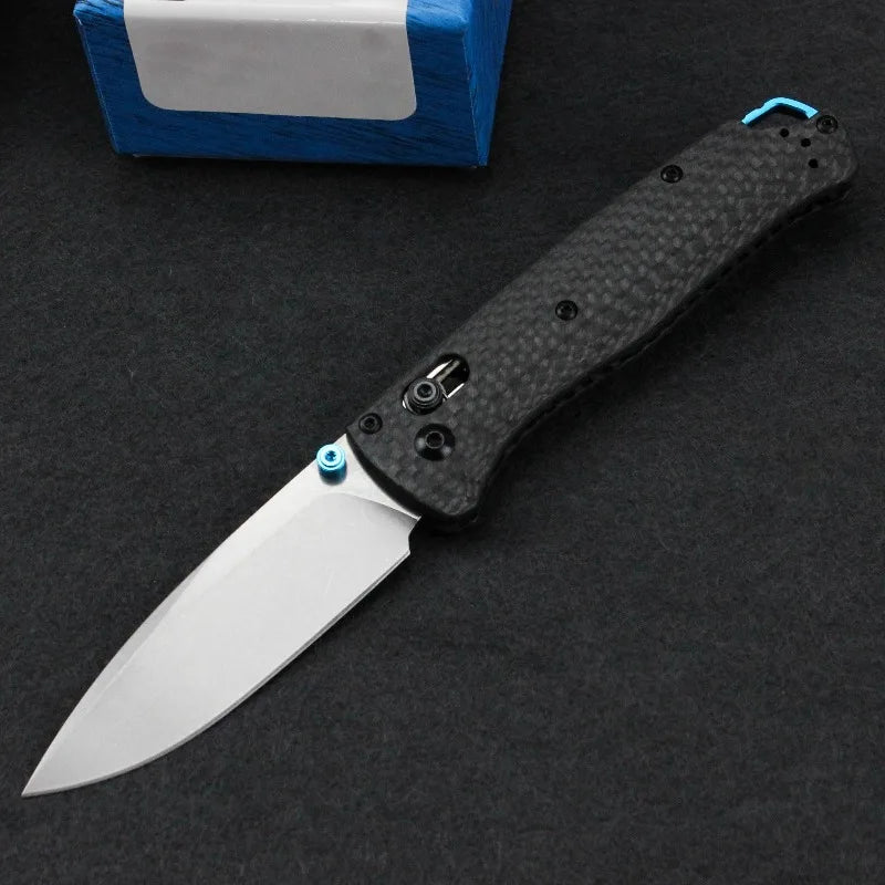 A black Damascus steel folding pocket knife with a silver blade and blue accents is displayed on a dark surface.
