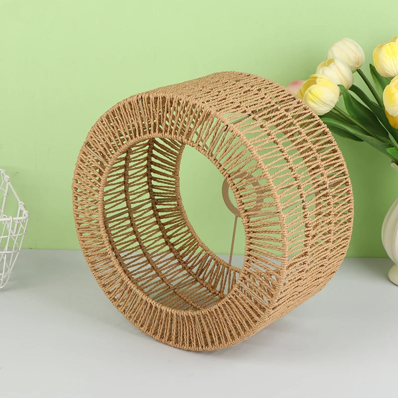 Pantalla de lámpara tejida de fibra natural hecha de cuerda de papel en diseño circular sobre fondo verde claro.