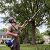 A man operates a professional 2-stroke gas pole saw for tree trimming in a grassy outdoor setting.