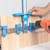 A hand uses a blue adjustable cabinet hardware installation jig to mark or align components on a wooden board.