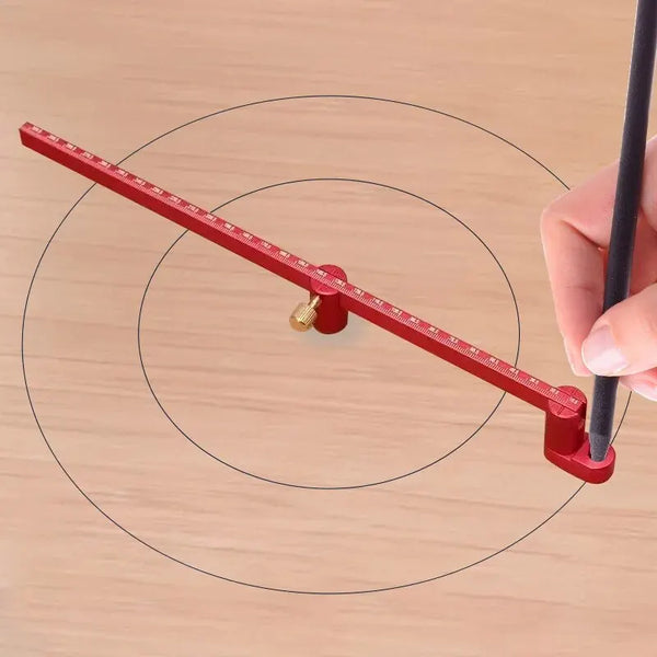 A hand holds a red precision drawing circle ruler with markings, demonstrating its use on a wooden surface.