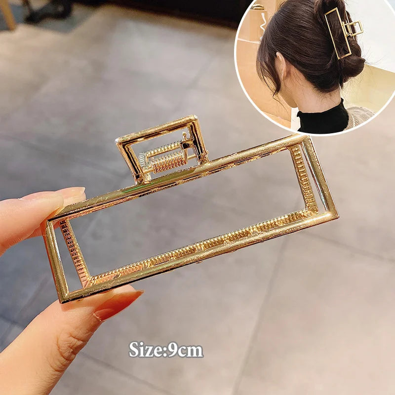 A hand holds an elegant gold S-shaped metal hair clip, showing its size and detail.