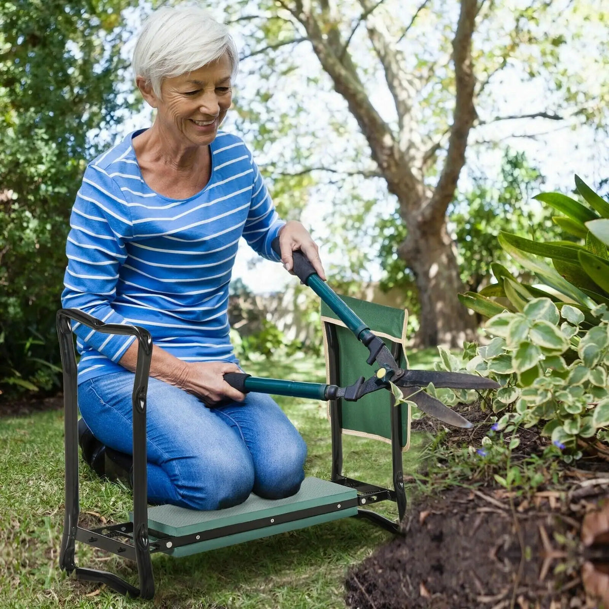 Eine ältere Frau sitzt auf einem schweren Gartenknienhocker in einem Garten.