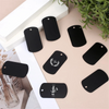 A collection of black aluminum metal stamping tags for crafts and keychains arranged on a light background.