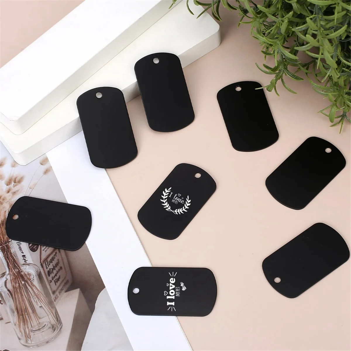 A collection of black aluminum metal stamping tags for crafts and keychains arranged on a light background.