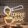A glowing neon sign shaped like a coffee cup and a coffee pot on a wooden surface.