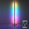A tall black floor lamp emitting a rainbow spectrum of light on a purple surface, next to a remote control.