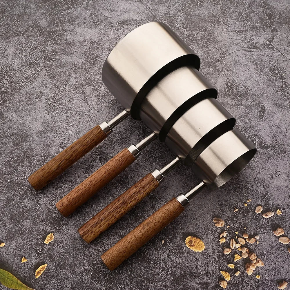 A set of stainless steel measuring spoons with wooden handles resting on a gray surface.