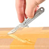A hand is holding a stainless steel folding keychain knife, positioned above a cardboard box.