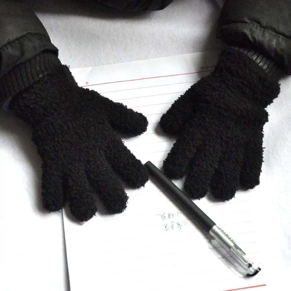 A pair of black plush full finger winter gloves resting on a piece of lined paper.