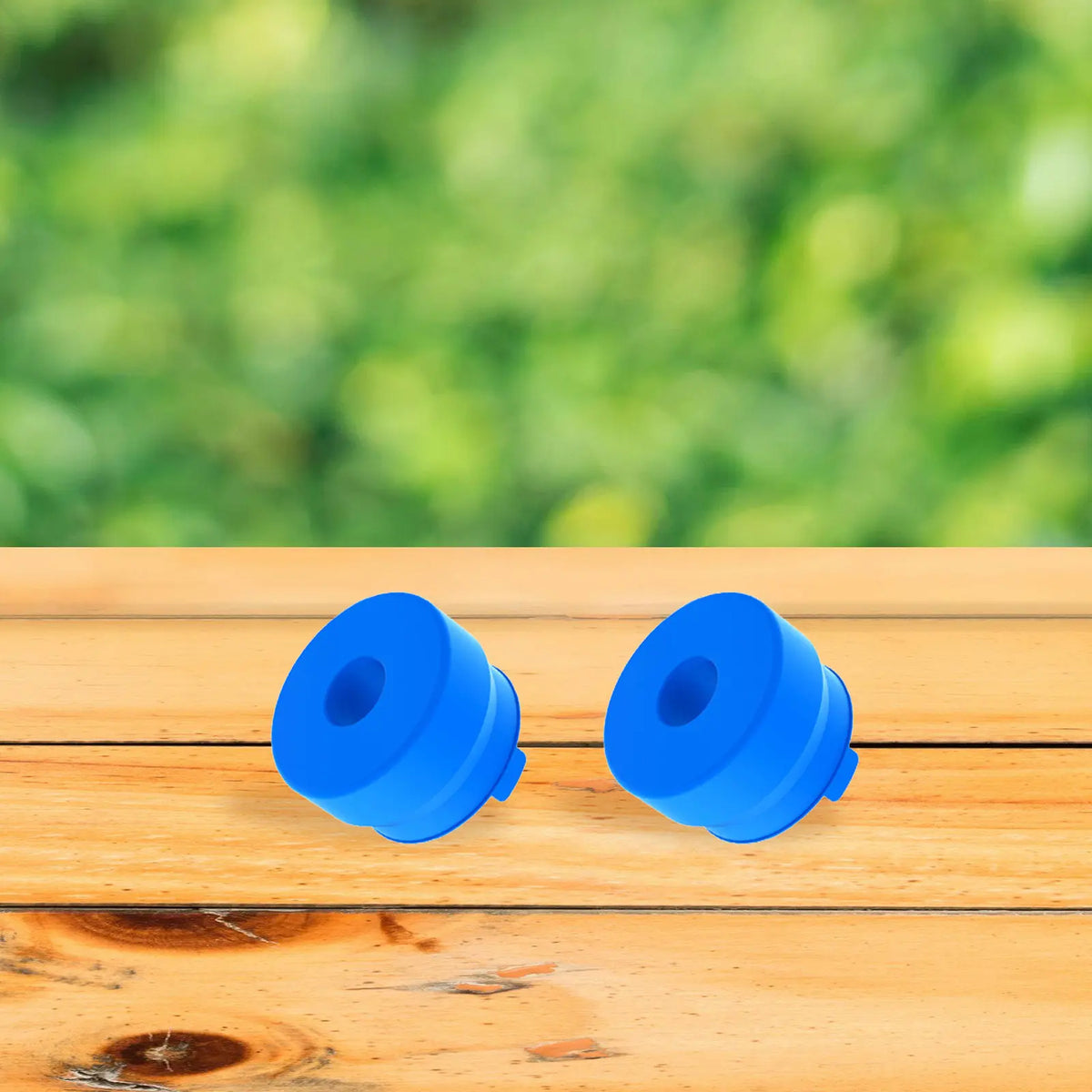 Dos tapas de botella reutilizables de silicona azul brillante sobre una superficie de madera clara.