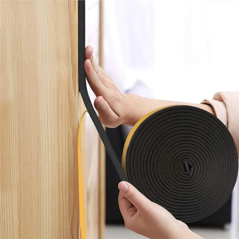 A hand is applying heavy duty rubber weather stripping seal tape to a wooden door frame.