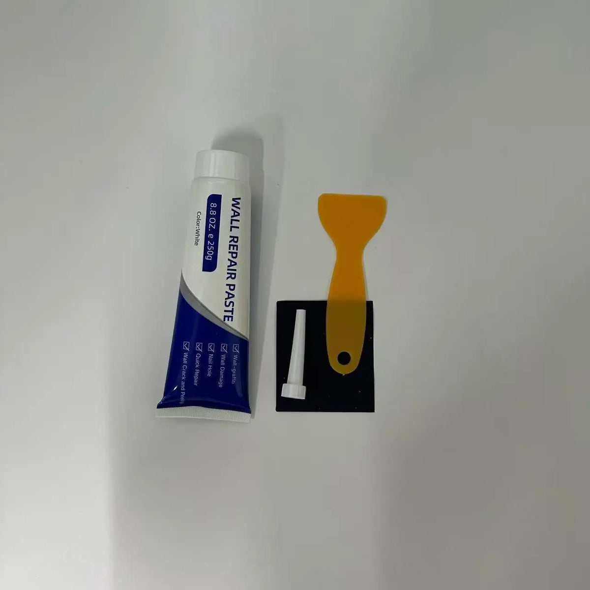 A white tube of wall repair paste with an orange applicator and a black holder.