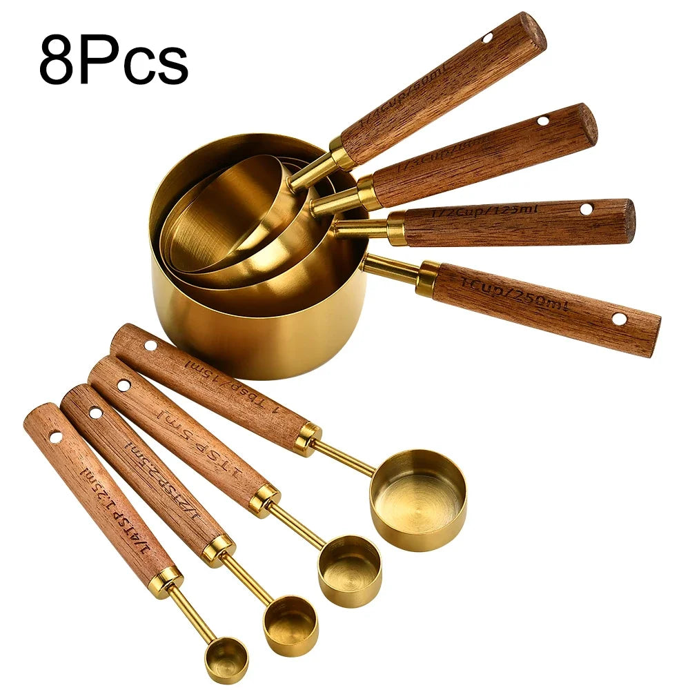 A set of eight stainless steel and wooden measuring spoons with gold accents.