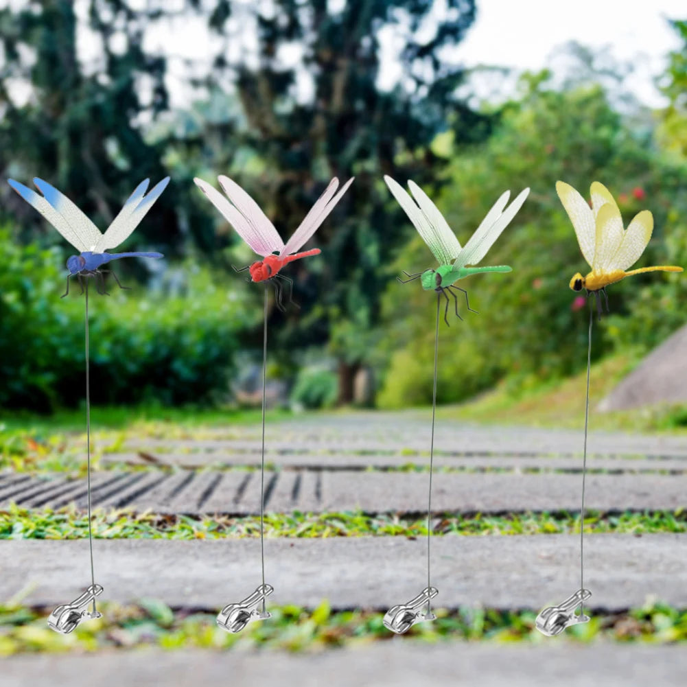 A realistic dragonfly clip with iridescent wings is displayed hanging from a thin wire in a garden setting.