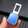 A hand holds a silver seatbelt clip extender with a blue plastic insert against a dark background.