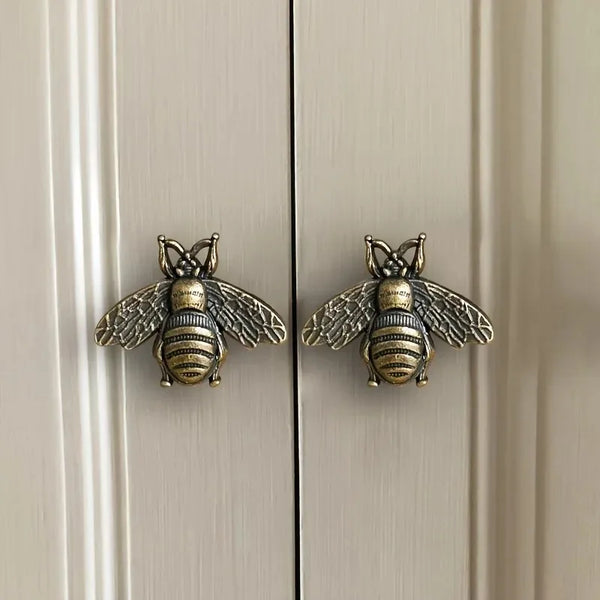 A pair of vintage brass bee cabinet handles or retro bar drawer pulls mounted on a white door.