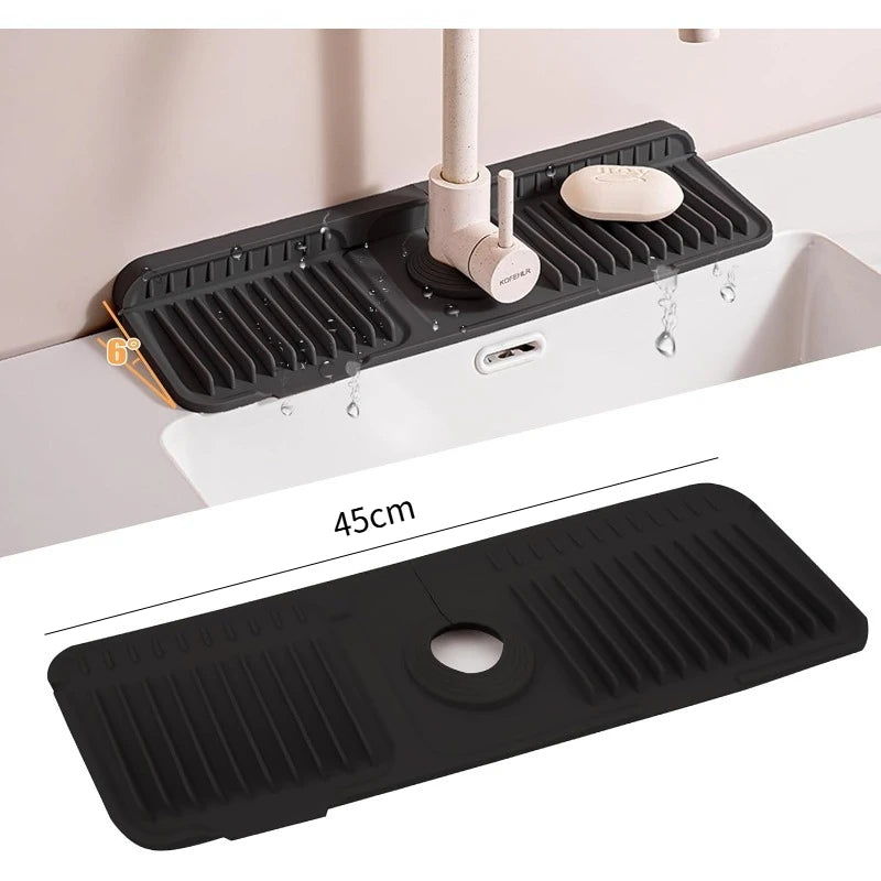 A black silicone sink splash mat with a drain and a small soap dish is shown in use on a white sink.
