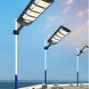 An outdoor solar motion sensor LED light fixture mounted on a pole, illuminating a paved walkway.