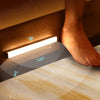 A wireless LED motion sensor night light is mounted under a cabinet, illuminating a textured surface with a 120-degree beam.