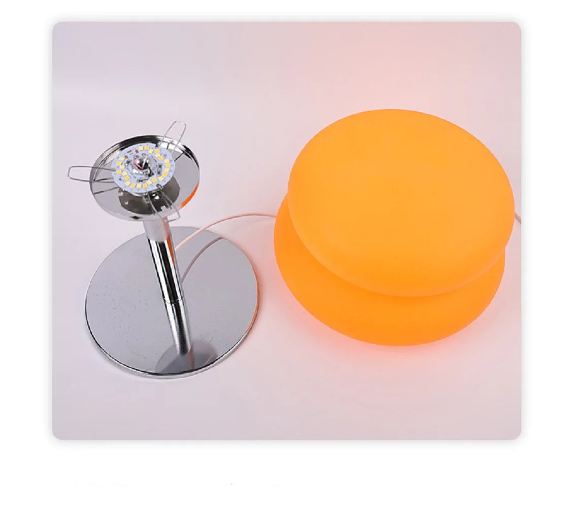 Lámpara de noche regulable de color crema con base plateada y pantalla esférica naranja.
